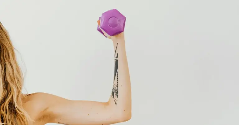Forearm with a small tattoo lifting a purple dumbbell.
