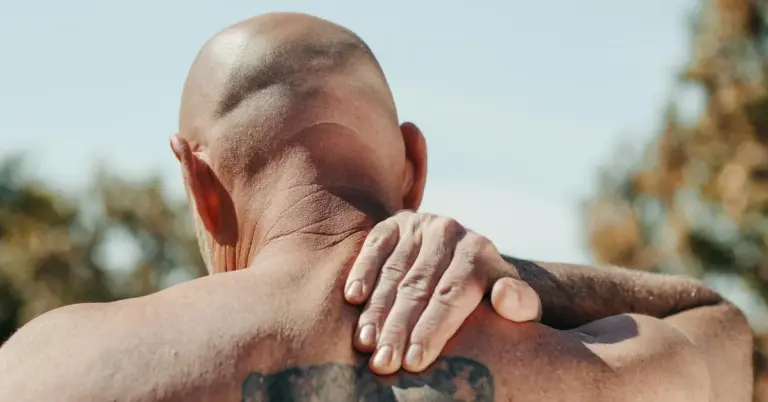 Back view of a shirtless man with a tattoo on his upper back, with a hand resting on his shoulder