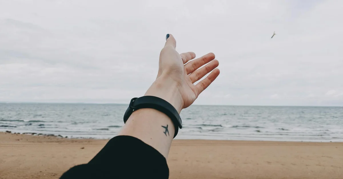 Wrist with a small star tattoo held up toward the ocean on a sandy beach