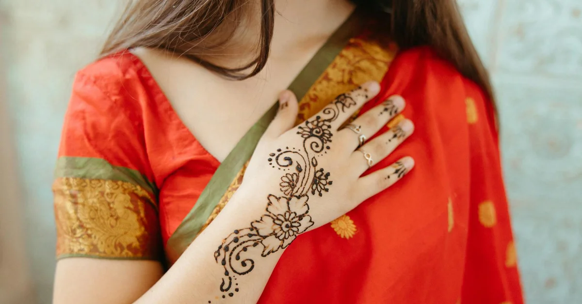 Close-up of a woman's hand and forearm with an intricate henna design, wearing a red traditional garment.