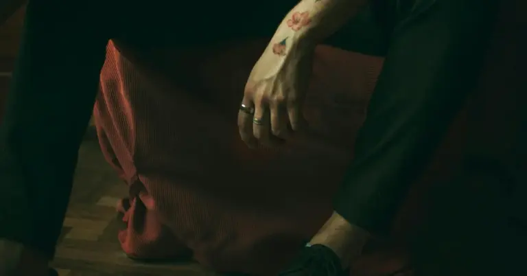 Close-up of a forearm with a small tattoo visible, resting on a knee in low light, illustrating the challenging context of blackout tattoo removal.