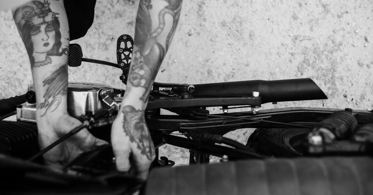 Black-and-white close-up of tattooed limbs resting on mechanical equipment, suggesting contemplation about removal.