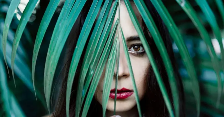 Close-up of a woman's face partly obscured by green tropical leaves