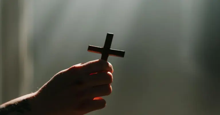 A hand gripping a small cross silhouette against a soft, blurred background.