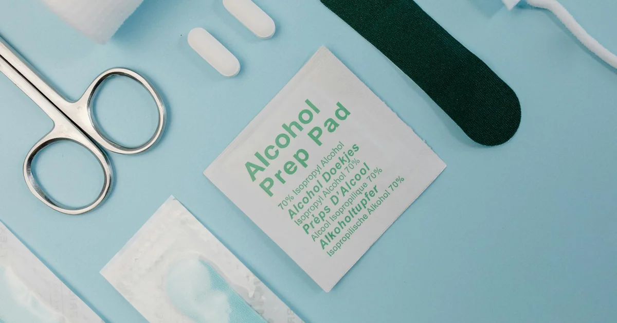 Medical supplies for tattoo removal aftercare on a blue surface, including an alcohol prep pad and stainless steel scissors