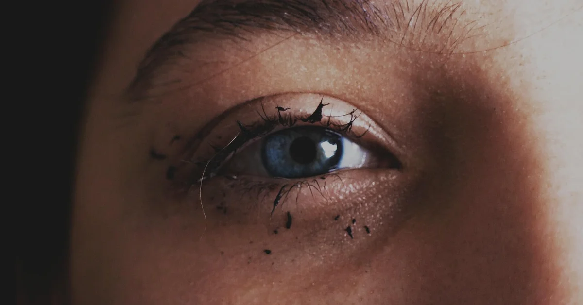 Close-up of an eye with smudged makeup and small marks around the eyebrow area, highlighting risks of at-home eyebrow tattoo removal.
