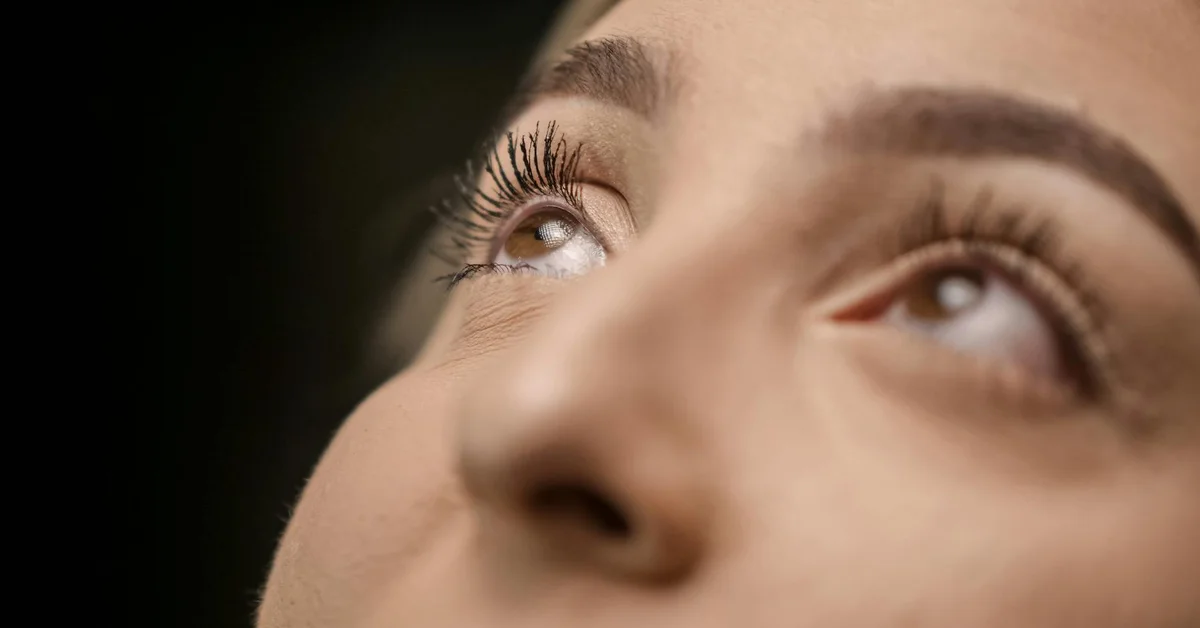 Close-up of a person's eye and eyelid, looking upward, with visible lashes
