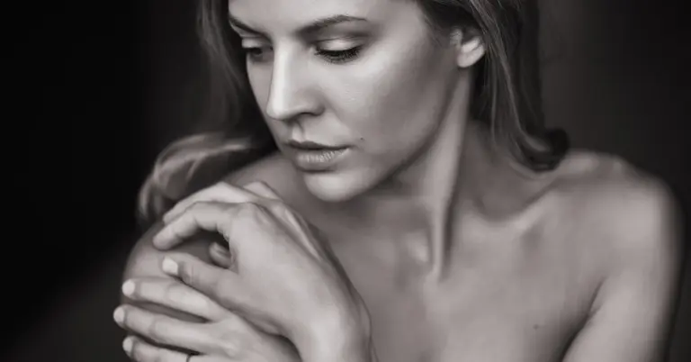 Black-and-white close-up portrait of a woman looking downward, with bare shoulders visible.