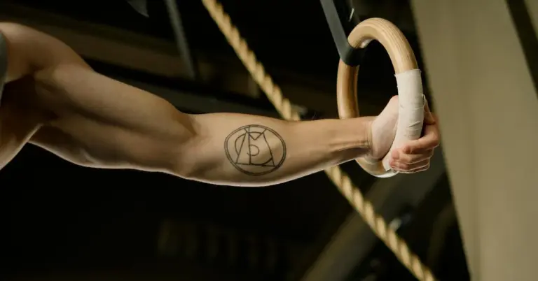 Forearm tattoo of a circle-A symbol on the inner arm, with a hand gripping a gymnastic ring.