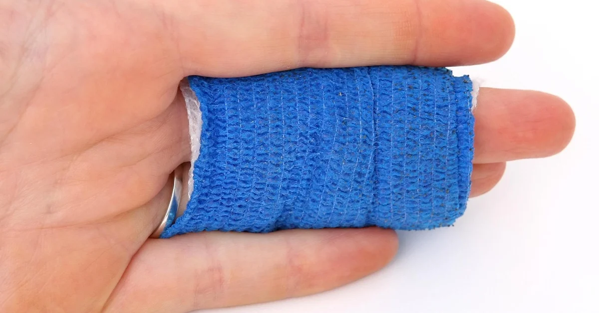 Close-up of a finger wrapped in a blue gauze bandage, illustrating ongoing healing after tattoo removal.