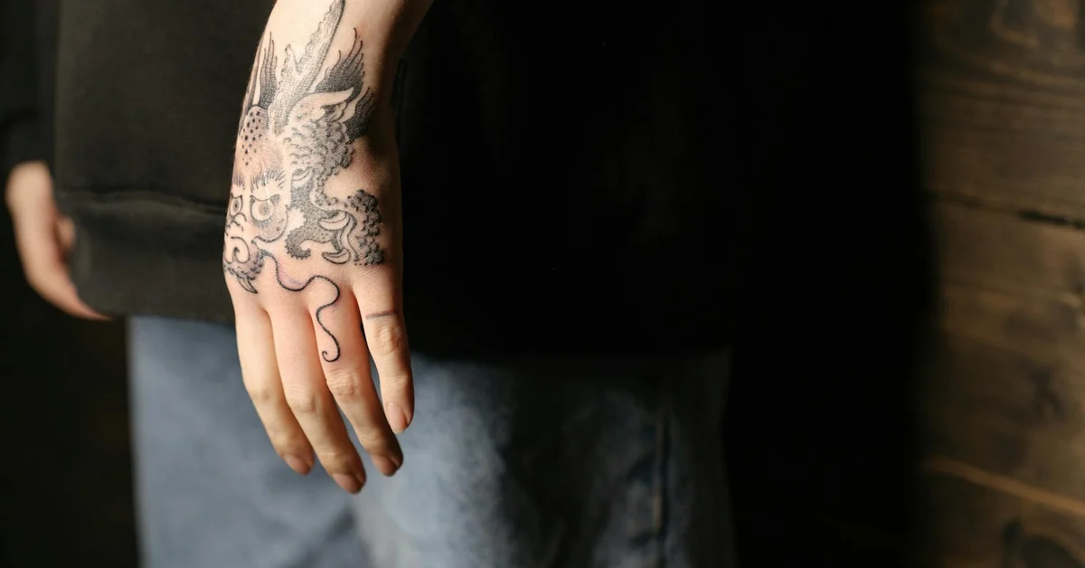 Close-up of a tattooed hand with an intricate dragon design, illustrating the topic of fingerprint tattoos.
