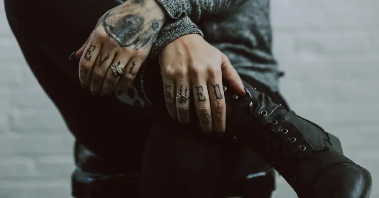 Close-up of tattooed hands resting on a boot, illustrating transformation and the context of free gang tattoo removal programs.