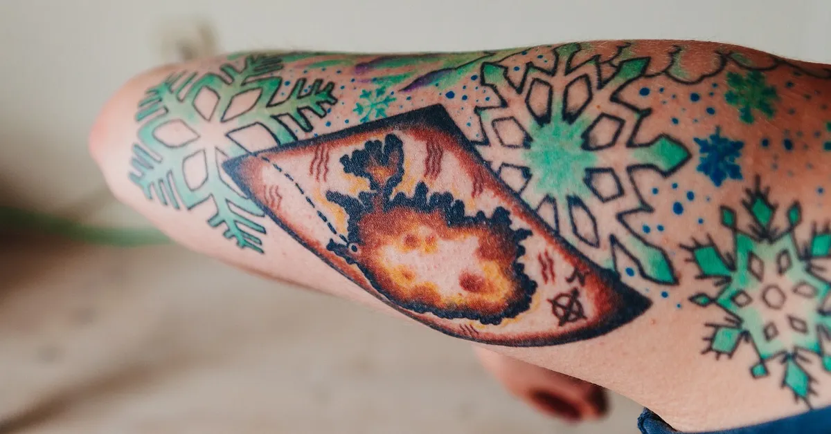 Close-up of a forearm with colorful tattoos featuring geometric shapes and snowflake patterns.