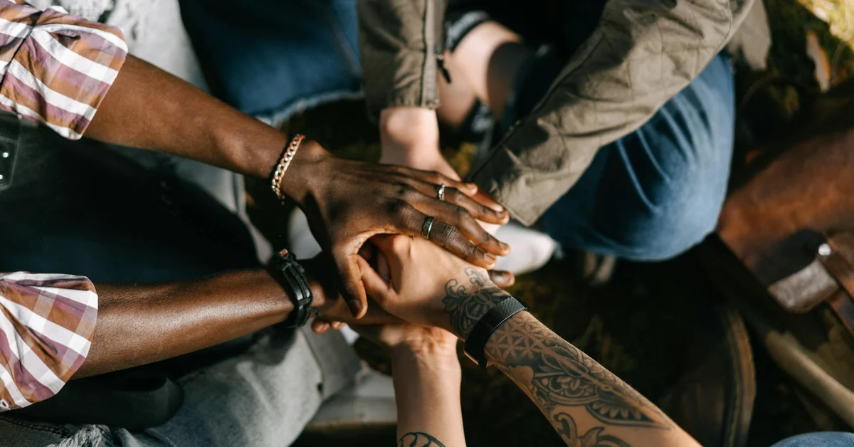Diverse group of people joining hands in a circle to symbolize teamwork and collaboration for starting a tattoo removal business.