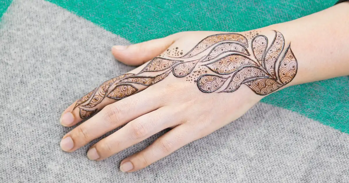 Close-up of a hand with a decorative, henna-inspired tattoo extending from the wrist to the fingers.