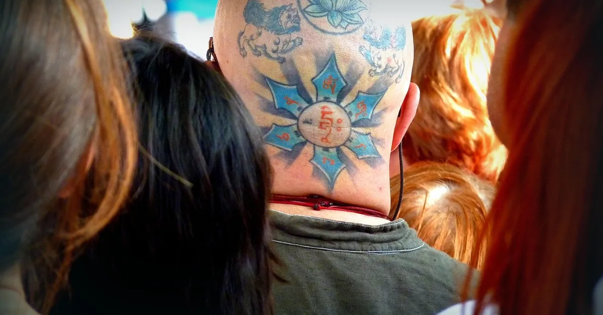Back of a person's head with a large blue starburst tattoo on the neck, surrounded by a crowd.