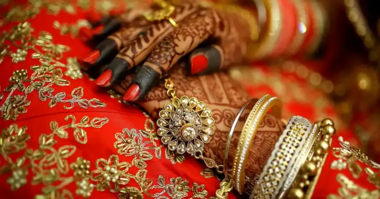 Close-up of hands with intricate henna tattoos and gold jewelry on red and gold fabric