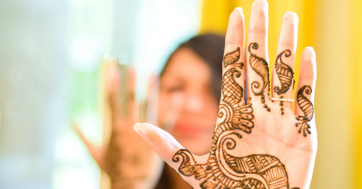 Close-up of a hand adorned with intricate henna designs held up with a blurred person in the background