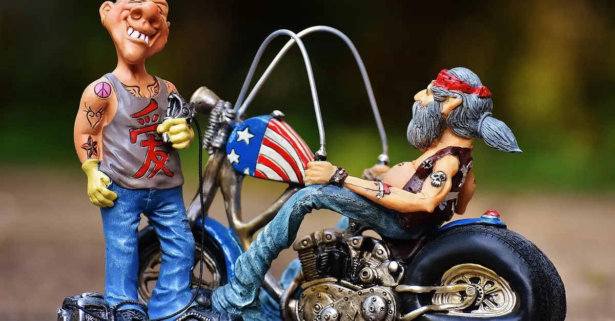 Two tattooed cartoon biker figurines posed on a small chrome motorcycle outdoors.