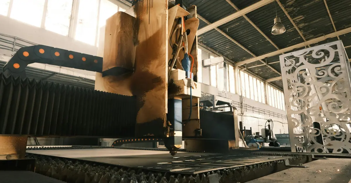 Industrial laser cutting machine with a large gantry in a factory, cutting metal sheets near an ornate decorative panel.