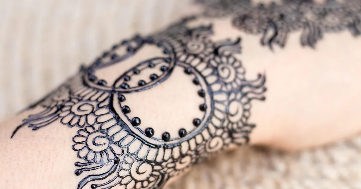 Close-up view of an ornate black tattoo pattern on skin featuring circular motifs and floral filigree.