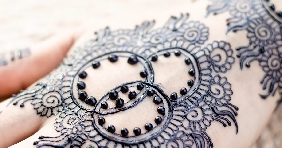 Close-up of a detailed black lace-inspired tattoo on skin with circular loop motifs and floral patterns.
