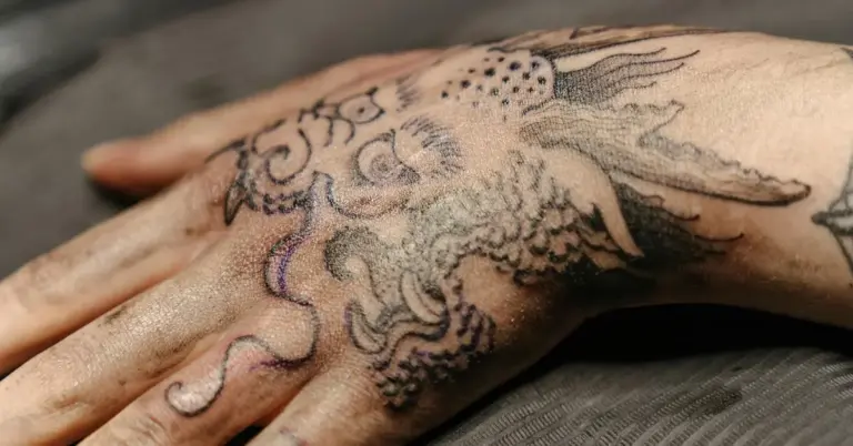 Close-up of a hand with a detailed black ink tattoo of a sea creature, showing intricate linework and shading.