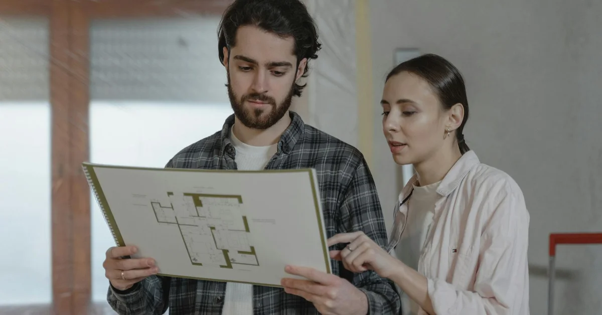 Two technicians review a schematic on a large board, discussing requirements and diagnosing issues.