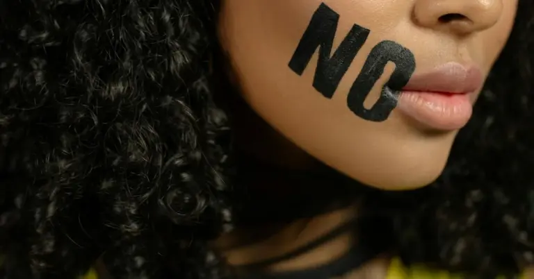 Close-up of a person with bold black letters 'NO' painted across the lips.
