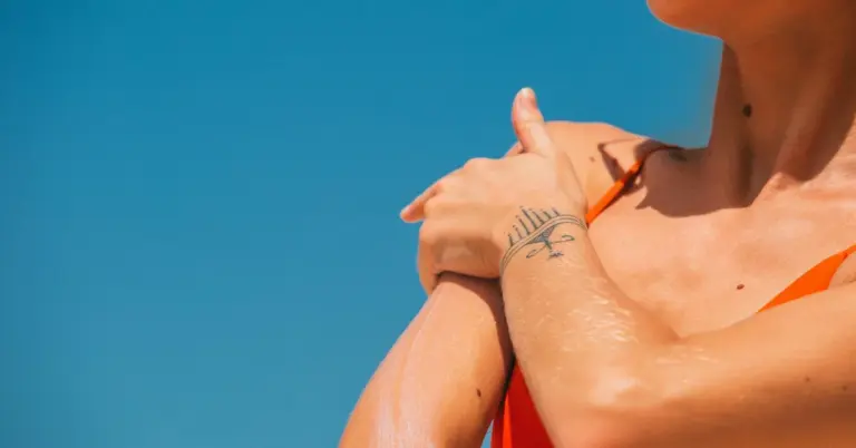 Close-up of a forearm with a small eye-and-crown tattoo against a clear blue sky.