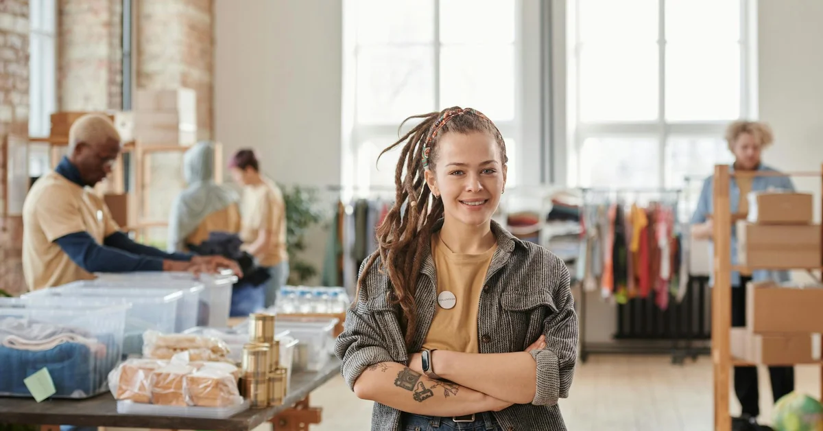 Portrait of a smiling woman standing in a bright, casual retail space with arms crossed, conveying confidence and readiness for a tattoo removal consultation.