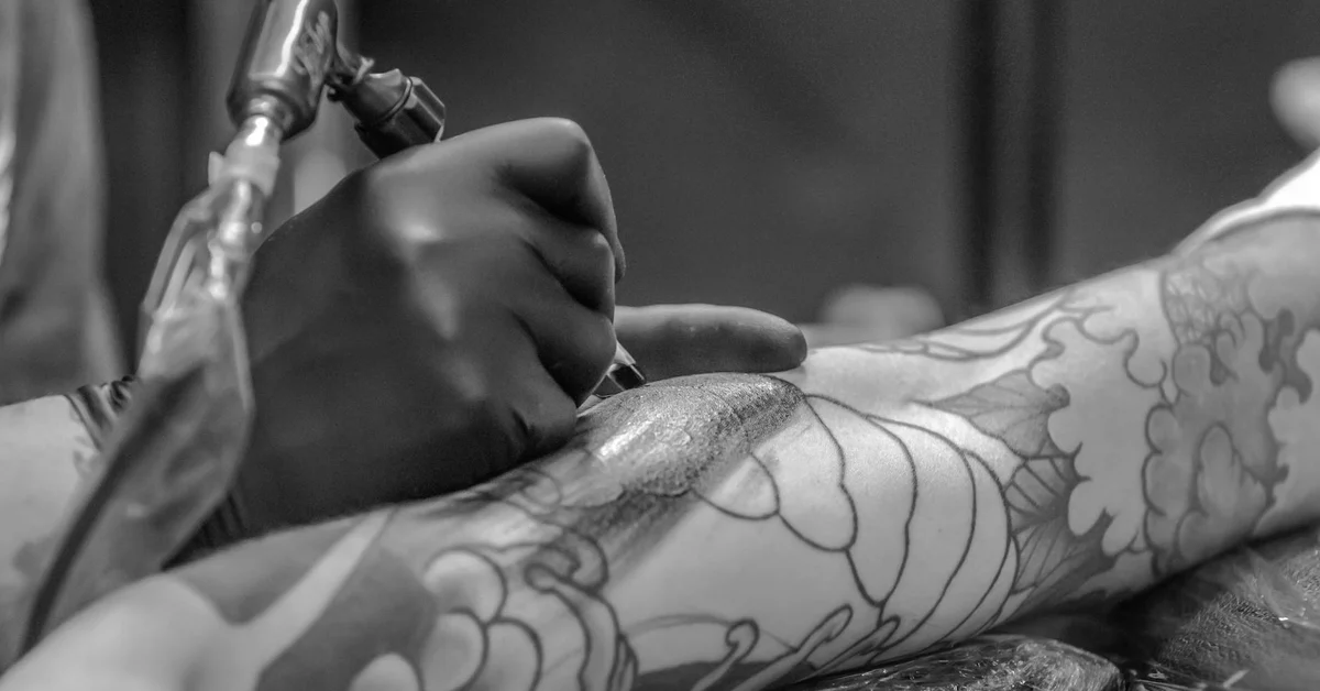 Close-up of a forearm with a tattoo being treated by a laser device during a tattoo removal session.