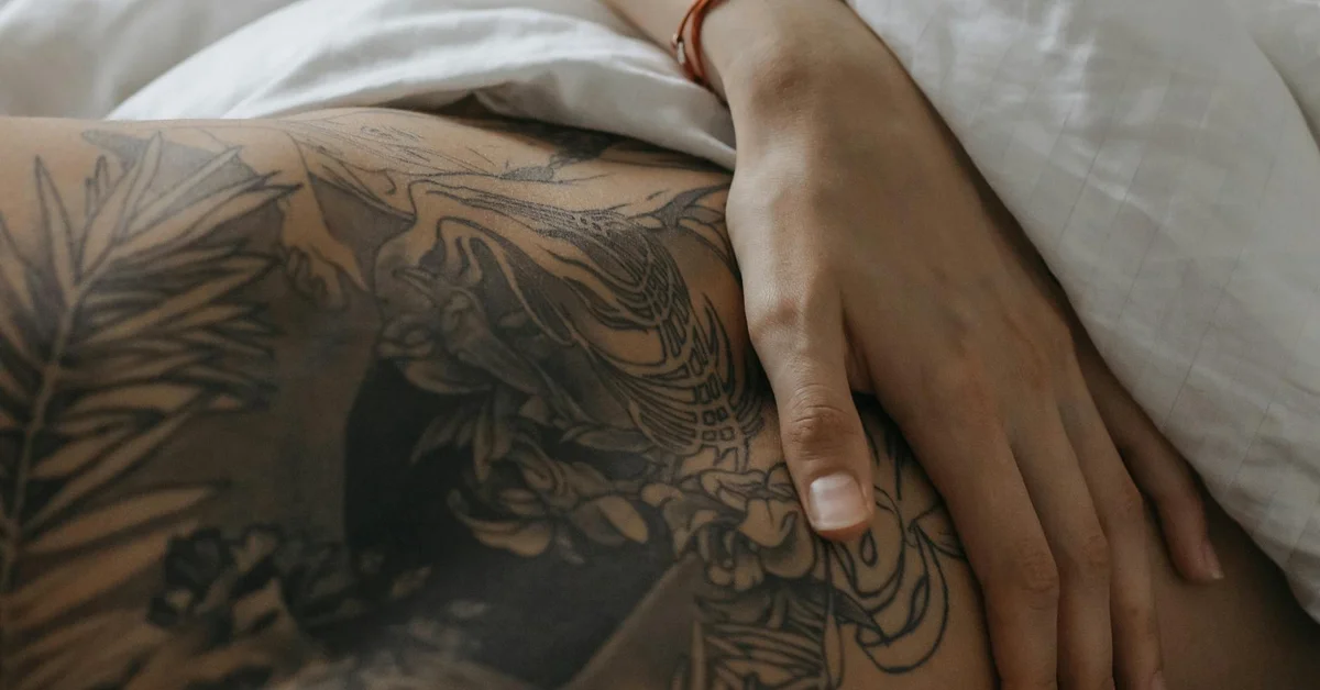 Close-up of a forearm with intricate tribal-style tattoos resting on a bed.