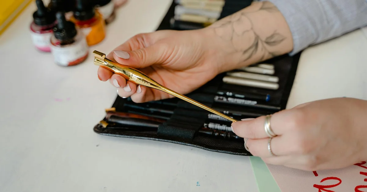 Close-up of a tattoo artist's hands preparing a cartridge needle above a tray of ink bottles on a clean workspace.