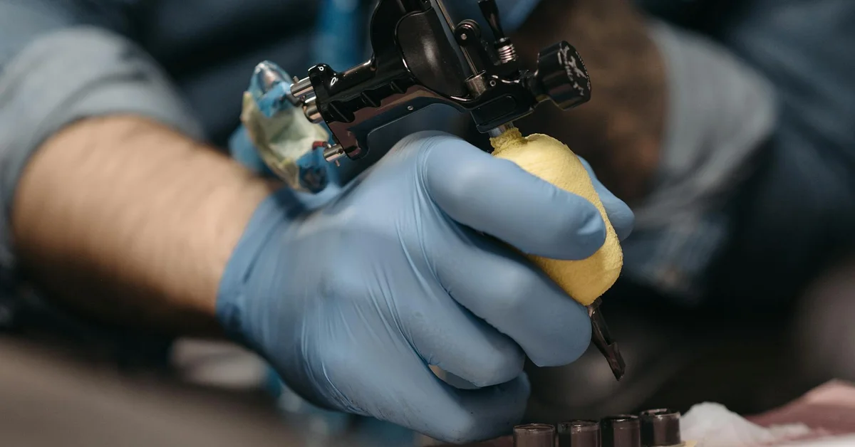 Close-up of a tattoo machine in gloved hands performing a procedure.