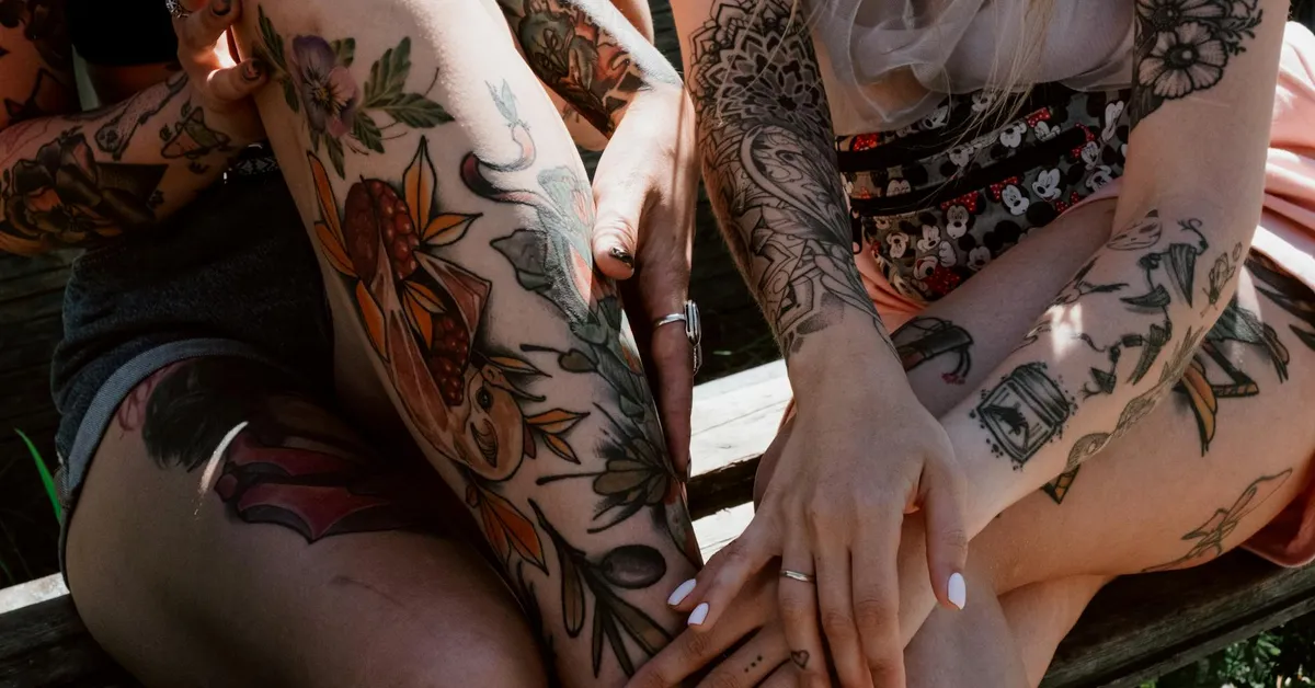 Close-up of multiple tattooed arms and legs resting on a wooden surface, displaying colorful designs.