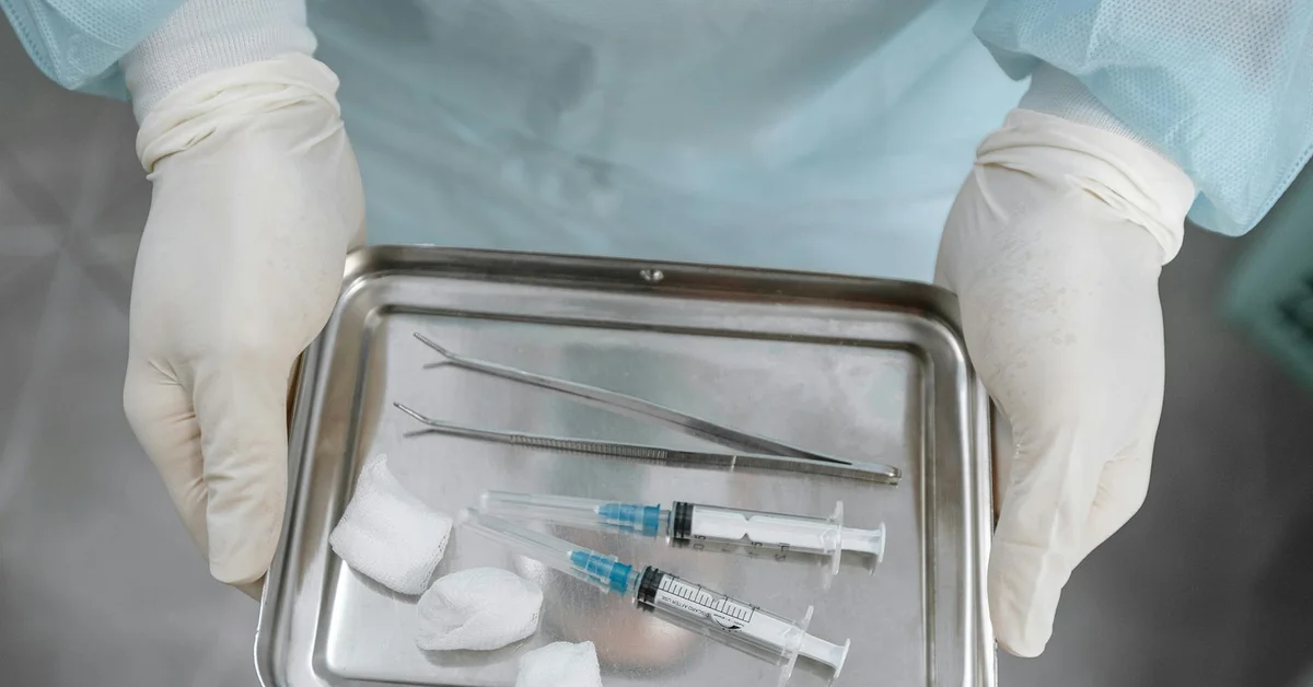 Sterile surgical tools and syringes laid out on a metal tray in a clinical setting, prepared for tattoo removal anesthesia.
