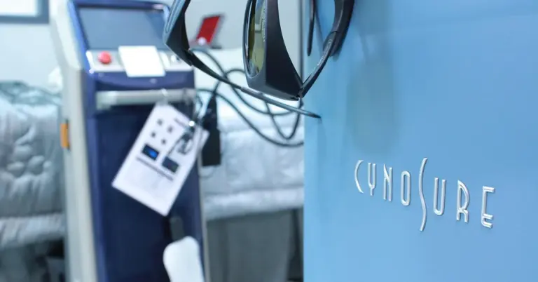 Close-up view of a tattoo removal clinic bed and laser equipment in a blue-walled treatment room.