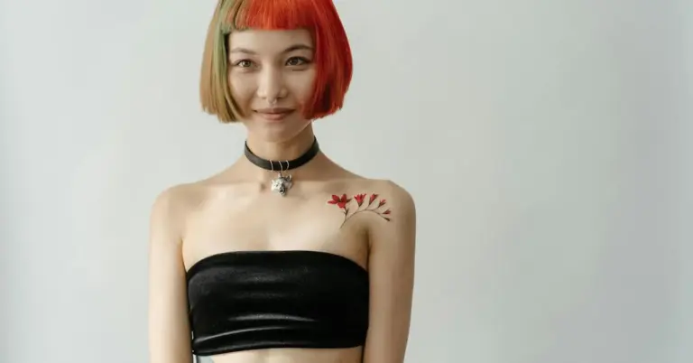 Person with a small red floral tattoo on the shoulder, wearing a black strapless top and a choker.