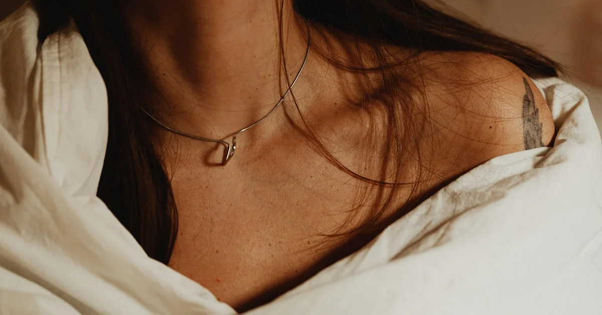 Close-up of a person's neck with a delicate necklace and white clothing, conveying calmness and precision.