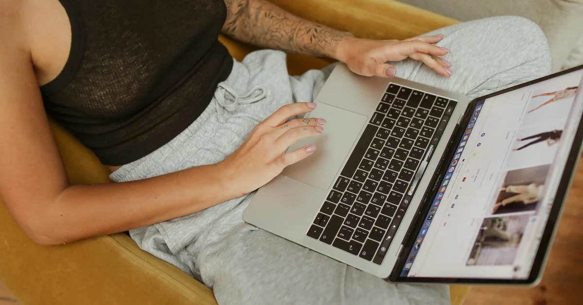 Top-down view of a person sitting on a couch with a laptop, researching marketing ideas related to tattoo removal clinic partnerships and referrals.