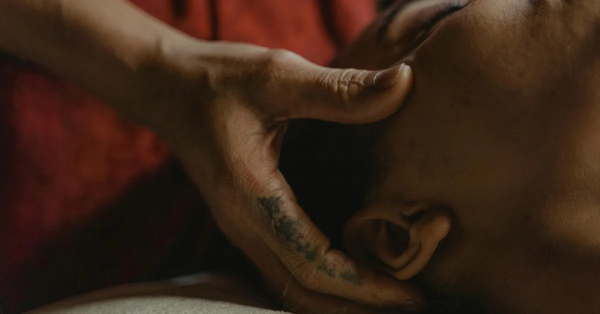Close-up of a tattooed forearm resting against a client's head during a skincare procedure, illustrating careful handling.