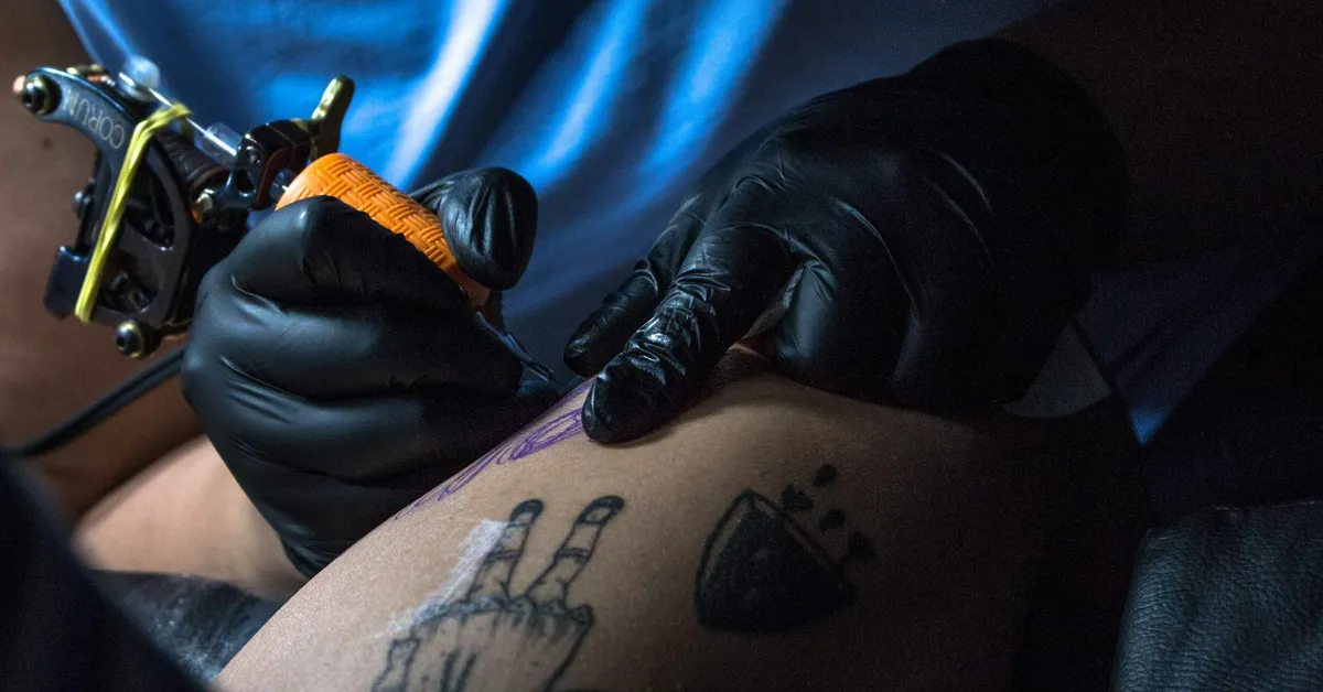 Close-up of a tattoo artist wearing black gloves using a tattoo machine on a client’s skin, illustrating a professional skin procedure.