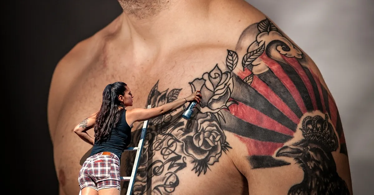 Person on a step ladder applying a protective dressing to a large chest tattoo on a shirtless man.