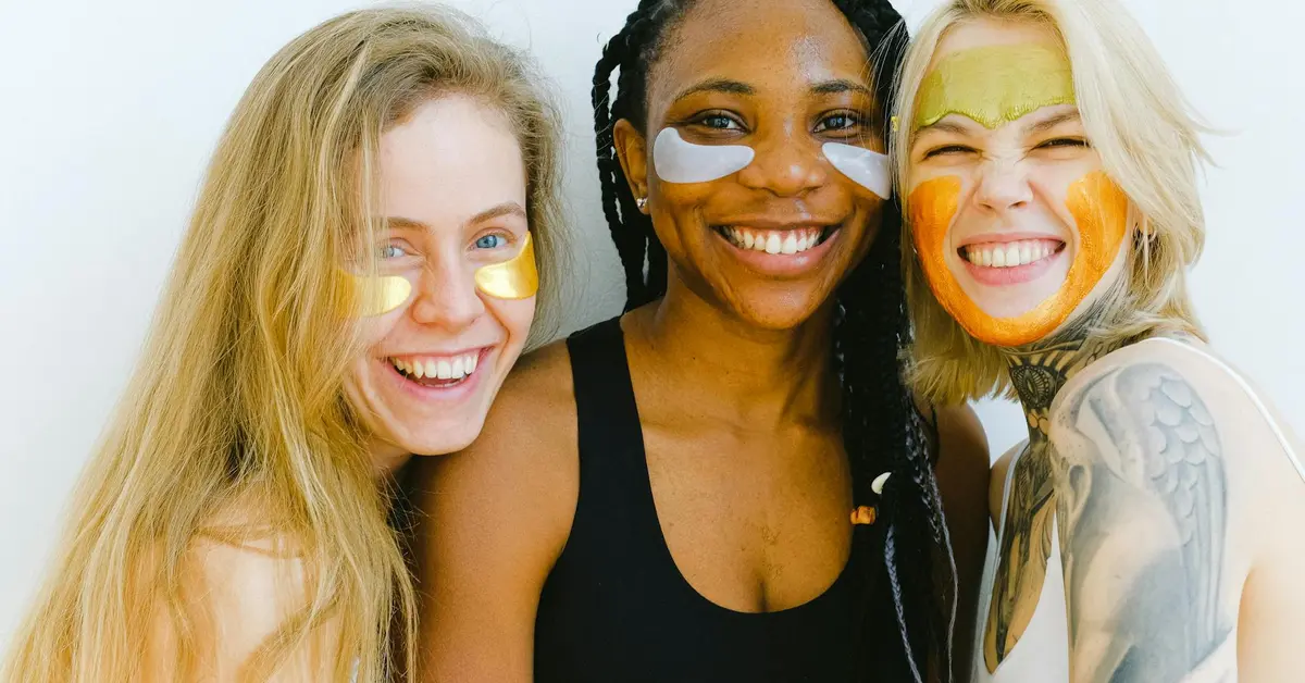 Three smiling women wearing colorful facial masks during a skincare session.