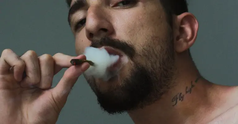 Close-up of a person with a neck tattoo exhaling smoke, viewed from the side.