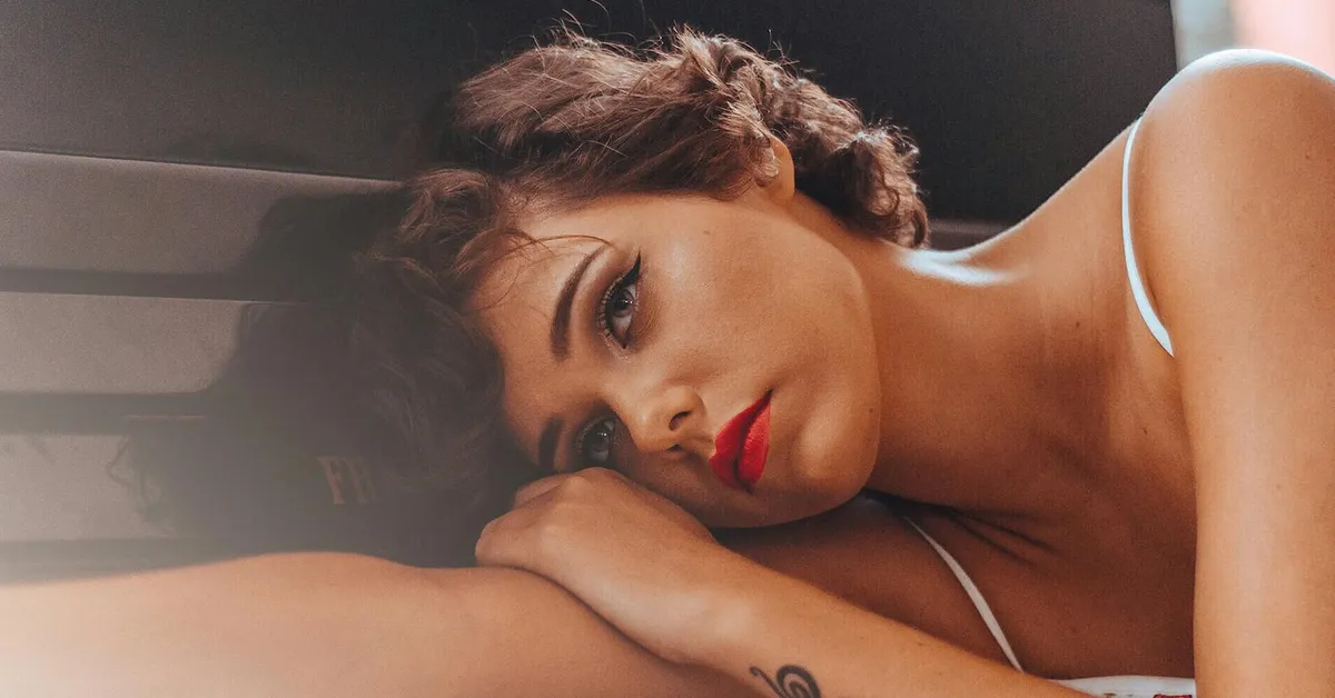 Portrait of a person resting their head on their arms, with soft lighting and bold red lipstick.